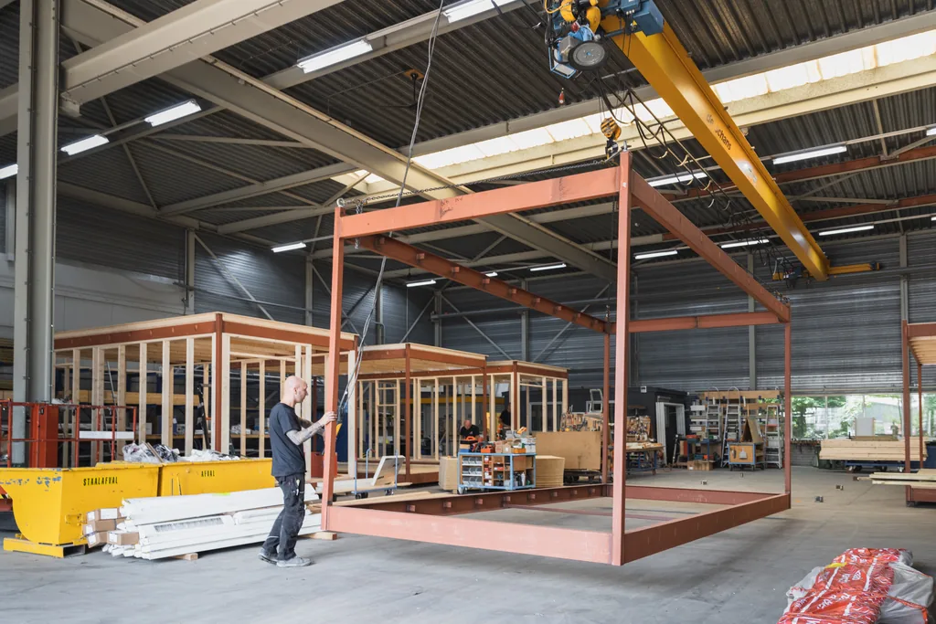 Stalen frame van een modulaire unit wordt in de fabricagefase door een werknemer met bovenloopkraan op de productielijn geplaatst