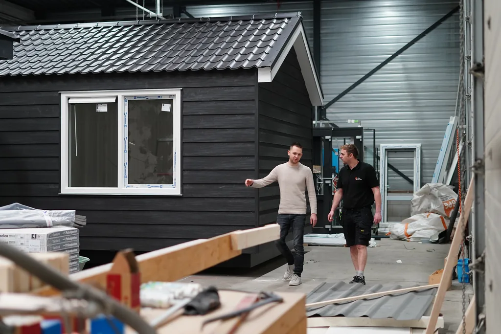 Twee De Schans medewerkers bij een afgewerkte modulaire unit met houten gevel en pannendak in de productiehal