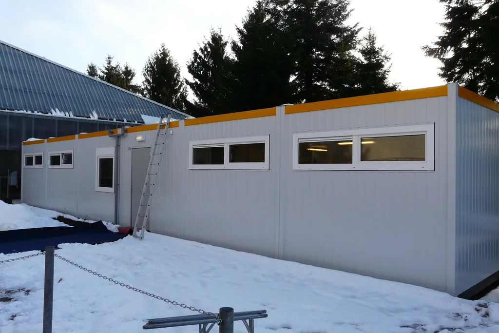 Modulaire tijdelijke gymzaal van De Schans bij sportcomplex met aluminium toegangsladder en grote raampartijen
